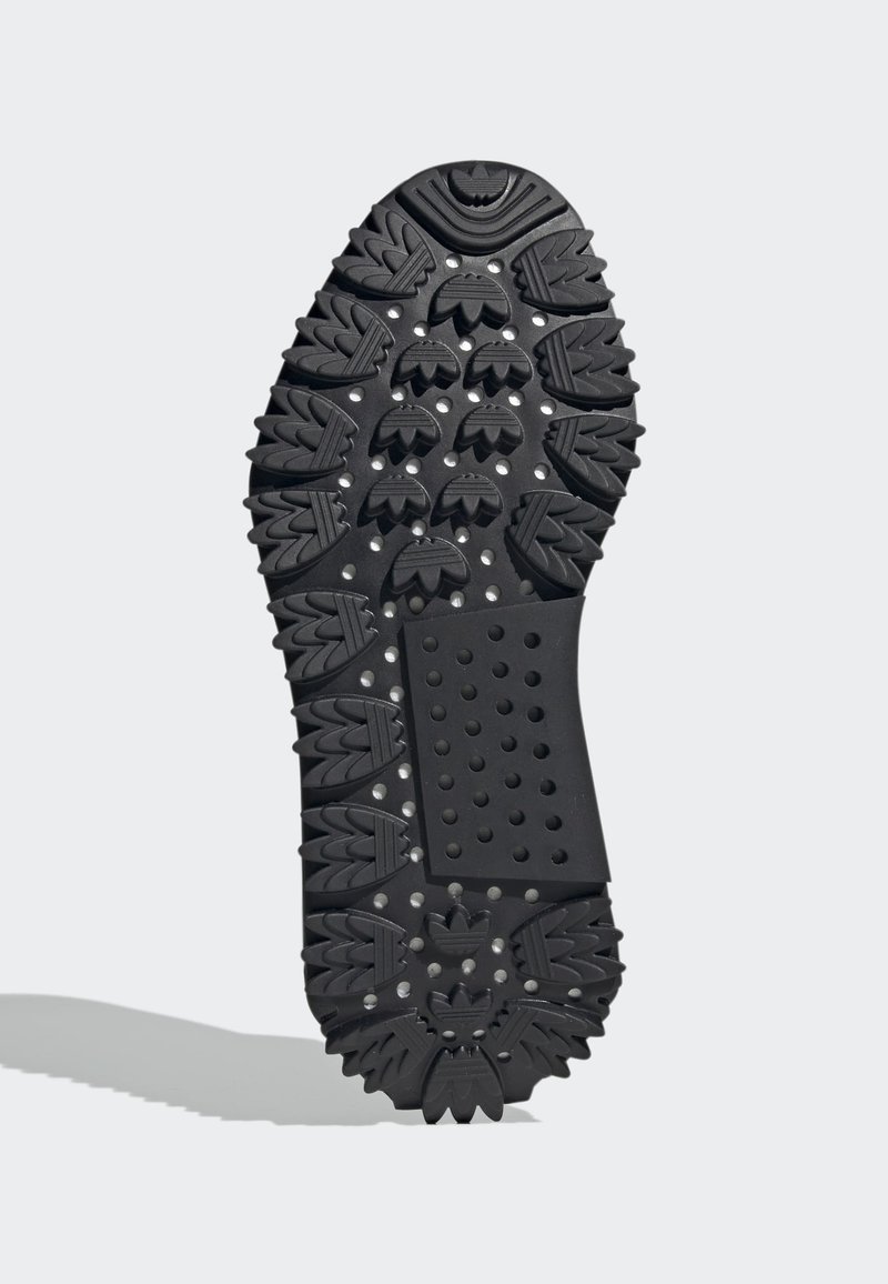 Suela de zapato de goma negra con un patrón de agarre que presenta acentos elevados y un área rectangular texturizada con perforaciones circulares.