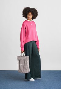 Rosa cropped sweatshirt med hvit logo, grønne plisserte vide bukser og lysegrå totebag med logo, båret med hvite joggesko.