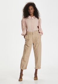 Blusa rosa chiaro strutturata con maniche a sbuffo, abbinata a pantaloni beige a vita alta, arrotolati alle caviglie, e sandali con tacco a blocco marroni.