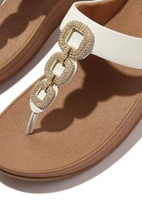 Witte teenslippers met drie gouden vierkante versieringen, gestructureerde bruine inlegzool en glad materiaal, dat geometrische accenten benadrukt.