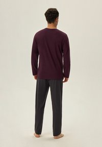 Męski zestaw odzieży domowej składający się z długiego rękawa, bordowej bluzki oraz szarych, luźnych spodni. Tkanina wydaje się być miękka i gładka.