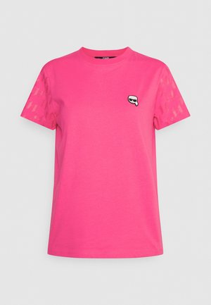 Camiseta de manga corta de color rosa brillante con un pequeño dibujo de cara en blanco y negro con gafas de sol en el lado izquierdo del pecho y mangas estampadas.
