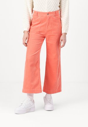 Coral corduroy wide-leg pants with two front pockets, topped with a metal button and contrasting stitching, paired with white sneakers.