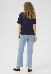 Top de manga corta en color navy con un corte relajado, combinado con jeans rectos de color azul claro que cuentan con bolsillos traseros y un dobladillo deshilachado, usado con bailarinas negras.