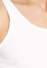 Weißes, geripptes Tanktop mit rundem Ausschnitt, das eine weiche Textur und engen Sitz zeigt. Oberkörper und Schulter sichtbar.