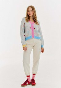 Szary kardigan w kolorowe kropki, różowe guziki i niebieskie mankiety, w zestawie z kremowymi spodniami i czerwonymi trampkami.