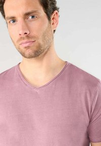 T-shirt a collo V in color rosa polveroso, realizzato in morbido cotone. Presenta una vestibilità morbida e una texture liscia con maniche corte e cuciture minime.