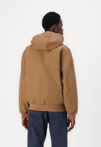 Sweatshirt à capuche marron avec des poignets et un ourlet côtelés. Le tissu semble doux, avec une coupe décontractée et une texture lisse. Coutures visibles.
