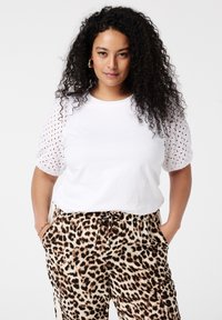 Weißes T-Shirt mit Spitzenverzierung an den Puffärmeln, kombiniert mit Leopardenmuster-Hosen. Weicher Stoff, entspannte Passform und elastischer Bund mit Kordelzug.