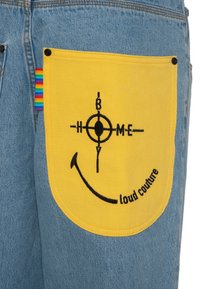 Denim shorts with a blue wash featuring a large yellow pocket. The pocket displays black embroidery of a circular design and text.