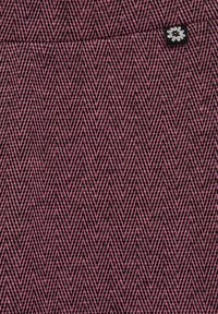 Tekstil s herringbone vzorom v rožnati in črni barvi. Ima strukturirano površino z majhno temno oznako, ki prikazuje cvetlični motiv.