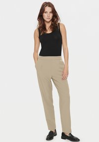 Pantalon beige ajusté avec poches latérales, associé à un top sans manches noir. Tissu lisse, coupe droite et accents matériels minimaux.