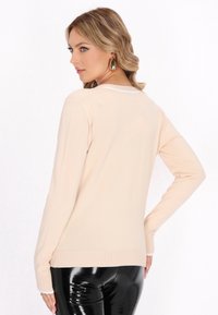 Jersey beige de manga larga con dobladillo y escote acanalados, que presenta una textura suave. Combinado con pantalones negros brillantes.