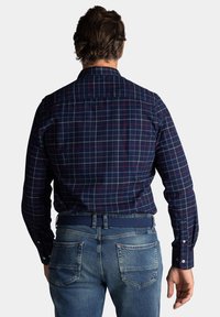 Marineblaauwe geruite shirt met rode en witte accenten, lange mouwen, met knoopmanchetten, gecombineerd met lichtblauwe denimjeans en een geweven riem.