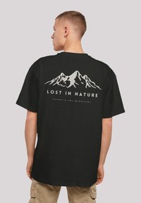 Schwarzes Baumwoll-T-Shirt mit einem weißen Berggrafik und dem Text "VERLOREN IN DER NATUR" auf der Rückseite. Kurze Ärmel, lockere Passform, Rundhalsausschnitt.