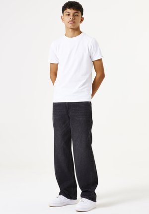 Witte katoenen T-shirt gecombineerd met donkere denim jeans en witte sneakers. De broek heeft een ontspannen pasvorm en zichtbare stikseldetails.