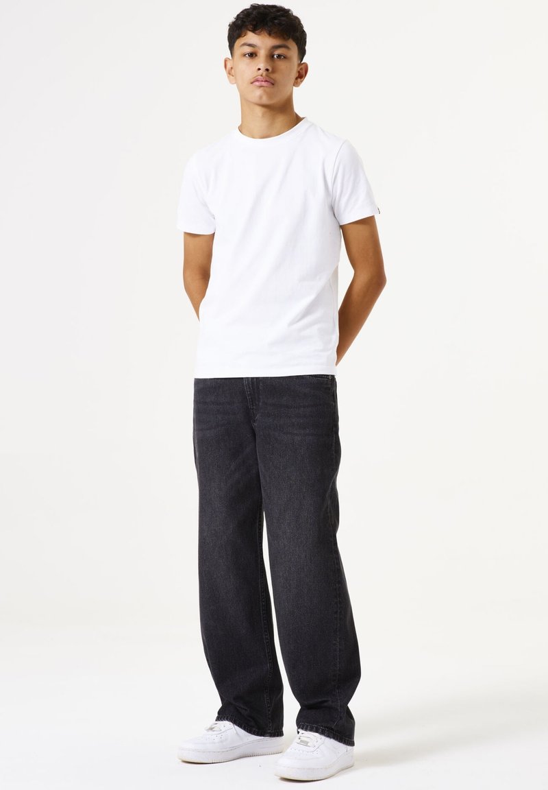 Camiseta blanca de algodón combinada con jeans de mezclilla oscura y zapatillas blancas. Los pantalones tienen un corte relajado y detalles de costura visibles.