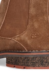 Botín de ante marrón con textura suave, paneles laterales elásticos y una suela de goma duradera con acabado estampado.