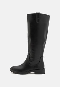 Bottes noires jusqu'aux genoux en cuir lisse avec un bout rond, un talon bloc et une languette pour un enfilage facile. Semelle en caoutchouc texturé.