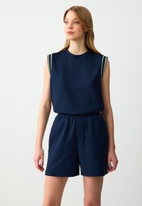 Completo activewear blu navy composto da un top senza maniche con accenti a strisce verdi e bianche e pantaloni corti con cintura elastica, realizzato in tessuto leggero.