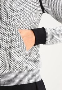 Svart och vit mönstrad sweatshirt med en texturerad yta, ribbade ärmslut och en sidoficka för händerna. Slimmad design.