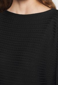 Svart texturerad topp med horisontella ränder och en bred halsringning. Tyget ser mjukt ut med en lätt ribbad yta.