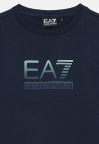 Marinebomull T-skjorte med reflekterende EA7-logo og "EMPORIO ARMANI" tekst trykket i midten, med rund hals og korte ermer.