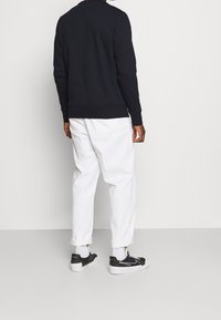 Navy sweatshirt with long sleeves, crew neck, and ribbed cuffs, paired with white trousers and black sneakers with white accents.