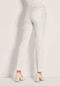 Weiße, hoch taillierte Hose mit schmal zulaufendem Bein und seitlicher Reißverschlusstasche, kombiniert mit beigen Wildleder-Pumps mit Blockabsatz.