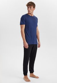 Maglietta blu navy a maniche corte con scollatura rotonda, abbinata a pantaloni jogger neri con polsini elasticizzati, indossati a piedi nudi.