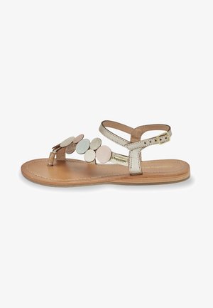 Brown flat sandal with multiple circular accents in soft pink, cream, and silver. Features an adjustable ankle strap and leather insole.