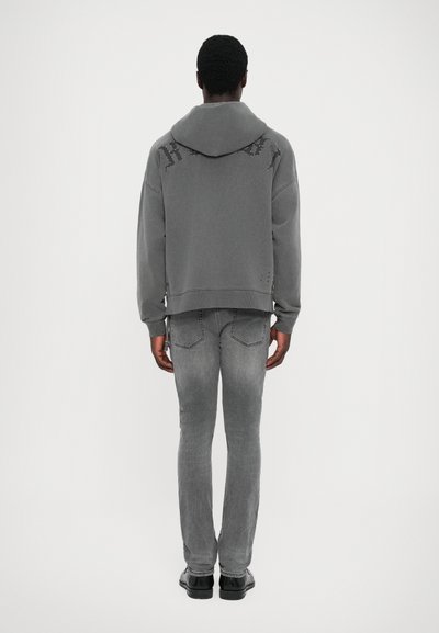 Grå hoodie med en texturerad huva, med fet lettering på baksidan, i kombination med grå jeans. Slät tyg, avslappnad passform, minimal detaljering.