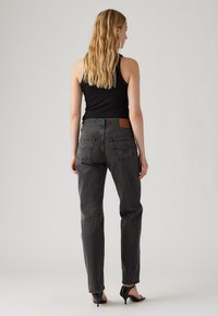 Grijze denim jeans met een hoge taille, rechte pijpen en een leren label op de achterkant. Gecombineerd met een zwart mouwloos shirt en zwarte hakken.