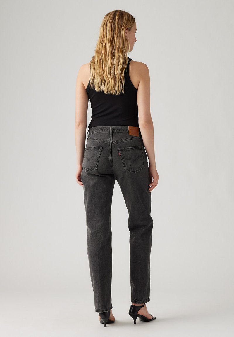 Jean en denim gris à taille haute, coupe droite, avec une patch en cuir dans le dos. Associé à un top sans manches noir et des talons noirs.
