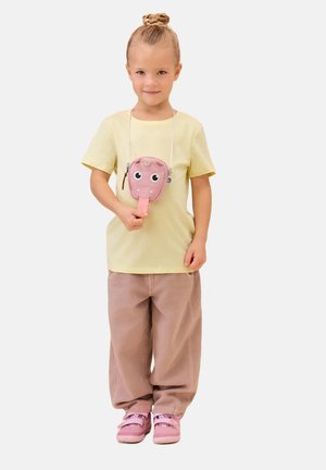 Young child with hair in a bun wears yellow t-shirt, loose beige pants, pink shoes, and a pink animal face pouch around the neck.
