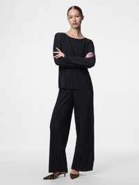 Top longo preto com pregas de manga longa emparelhado com calças largas de pregas do mesmo tecido. Tecido texturizado com um corte relaxado, apresentando um decote à barco.