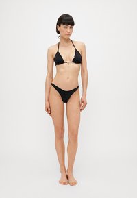 Black bikini set featuring a scalloped trim. The top has a triangular shape with halter neck ties, and the bottom is a minimalistic, low-rise style.