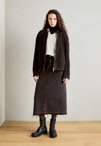 Veste en denim noir avec fermeture éclair argentée, pull gris, longue jupe en denim noir et bottes noires à lacets avec surface texturée et semelle robuste.