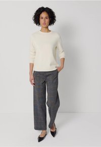Kremowy sweter z dzianiny, szerokie szare spodnie w kratę z kolorowymi akcentami i czarne baleriny na spiczastym nosku. Minimalistyczny design, miękka faktura.