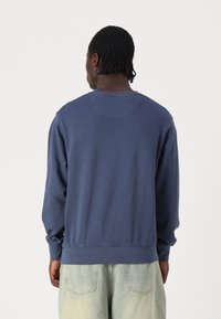 Navy blue sweatshirt with long sleeves and a round neckline. Soft fabric with a smooth texture. Back features a seamless yoke detail.