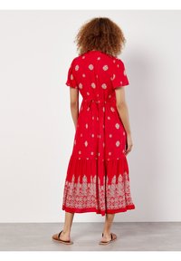 Rotes Baumwollkleid mit kurzen Ärmeln, tailliertem Oberteil, Kordelzug in der Taille und gestuftem Rock, der am Saum mit weißen Blumenmustern verziert ist.
