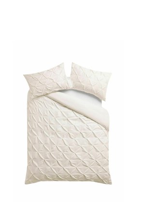 Bettwäsche in Cremefarbe mit strukturiertem Diamantmuster, inklusive eines teilweise zurückgefalteten Bettbezugs und zwei passenden Kissen.