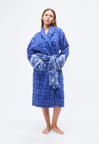 Μπλε μπουρνούζι από πετσέτα με μεγάλο επαναλαμβανόμενο μοτίβο λογότυπων, μακριά μανίκια με διακοσμητικές μανσέτες και ζώνη που δένει στο ίδιο σχέδιο.
