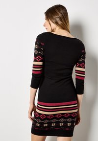Sukienka dzianinowa charakteryzująca się czarnym korpusem, wzorzystymi czerwono-beżowymi rękawami oraz kolorowym geometrycznym wzorem na dole. Dopasowany krój z rękawami o długości trzy czwarte.
