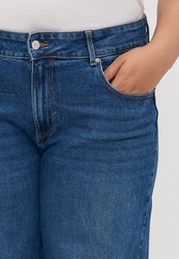 Blue denim jeans with a classic cut, featuring a zipper and button closure, two front pockets, and visible stitching details.