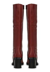 Térd fölé érő piros bőr csizmák, sima felülettel, fekete tömbtalppal és oldalsó cipzárokkal. Az összekötött varrások részletességet adnak.