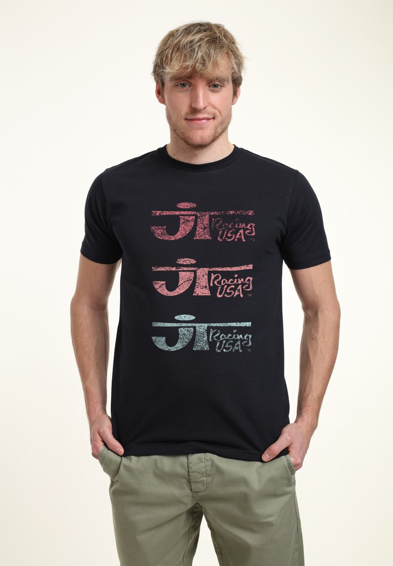 Schwarzes Baumwoll-T-Shirt mit drei übereinander gestapelten "Racing USA"-Logos in Rot, Pink und Hellblau mit einer strukturierten Oberfläche.