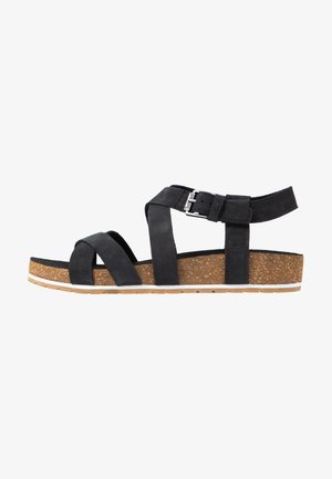 Black sandal featuring cross straps and a buckle closure. Cork footbed with rubber sole. Textured upper material. Lightweight design.