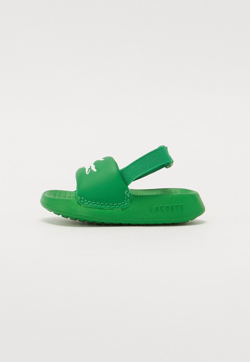 Green rubber slide sandal with a textured sole, featuring a strap at the back and a white logo on the front. Minimalist design, soft material.