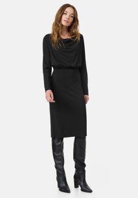 Zwart lange mouwen jurk met een cowl-halslijn en een elastische tailleband, gecombineerd met kniehoge zwarte laarzen, met een aansluitende pasvorm.